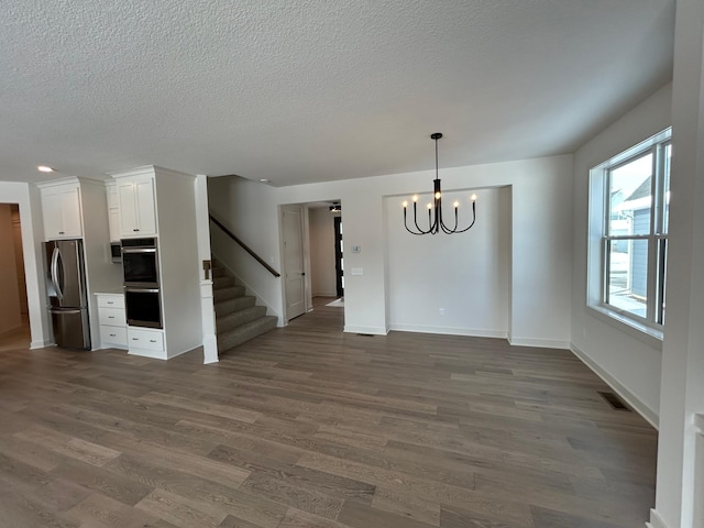 interior space with dark wood finished floors, a notable chandelier, visible vents, baseboards, and stairs