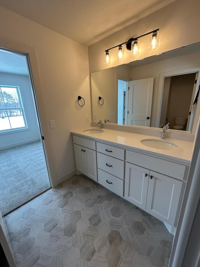 bathroom with a textured ceiling, double vanity, a sink, and toilet