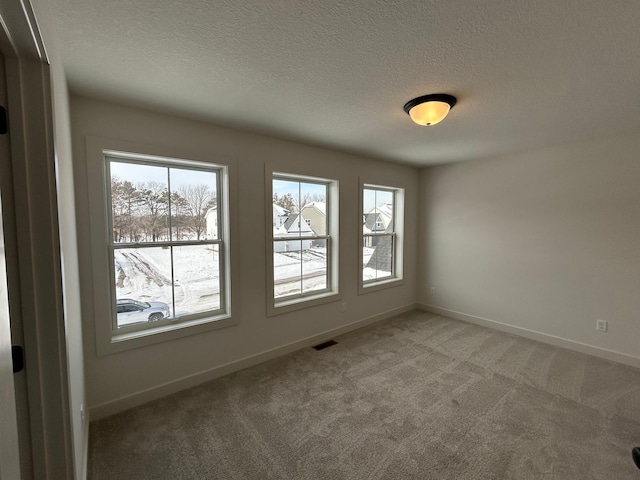 unfurnished room with carpet floors, baseboards, visible vents, and a textured ceiling