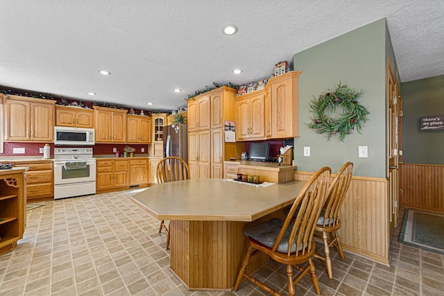 kitchen with built in desk, wood walls, a kitchen breakfast bar, white appliances, and a textured ceiling