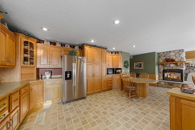 kitchen with a stone fireplace, a textured ceiling, and stainless steel fridge with ice dispenser