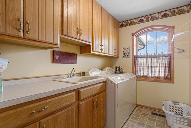 clothes washing area with sink, washer and clothes dryer, cabinets, and a textured ceiling