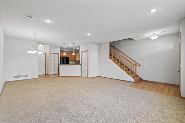 unfurnished living room with light carpet, visible vents, stairway, and a textured ceiling