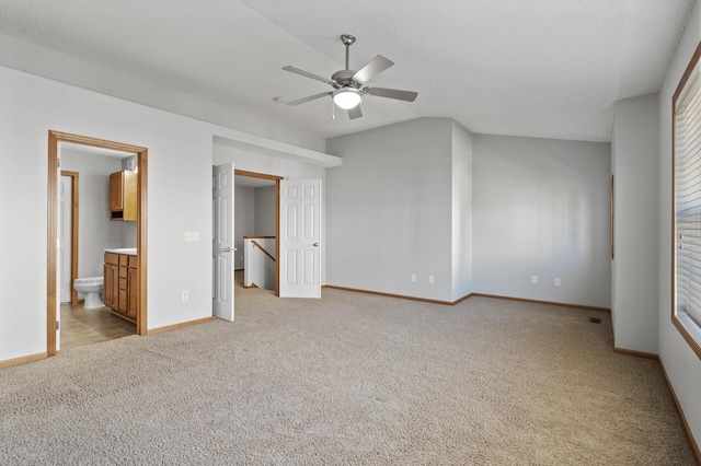 unfurnished bedroom with vaulted ceiling, light carpet, connected bathroom, and baseboards