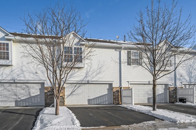 view of snow covered exterior featuring brick siding, an attached garage, and aphalt driveway