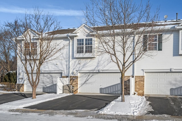 view of snow covered exterior with an attached garage, aphalt driveway, and brick siding