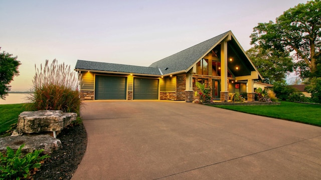 view of front of home featuring an attached garage, stone siding, driveway, and a front lawn