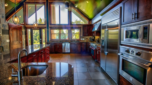 kitchen featuring pendant lighting, a sink, dark stone countertops, built in appliances, and dark tile patterned floors