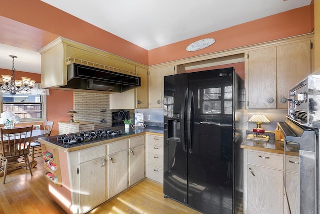 kitchen featuring light wood-type flooring, black appliances, under cabinet range hood, an inviting chandelier, and decorative backsplash