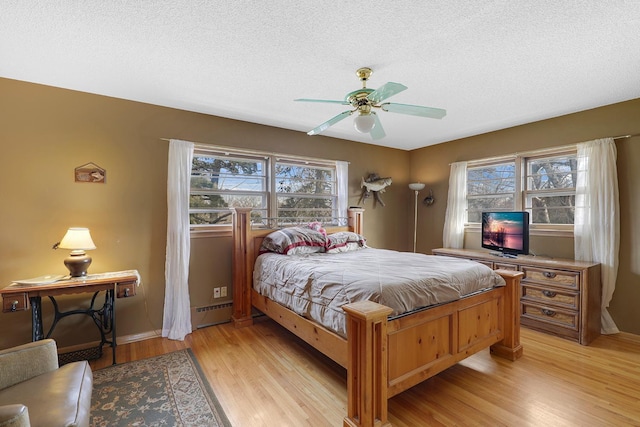 bedroom with a baseboard heating unit, a textured ceiling, light wood-style flooring, and a ceiling fan