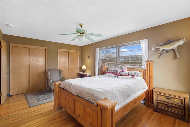 bedroom featuring light wood-style flooring, a textured ceiling, multiple closets, and ceiling fan