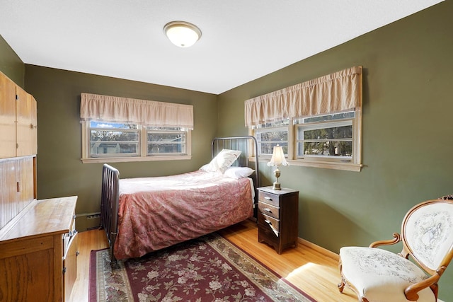 bedroom featuring a baseboard radiator, baseboards, and wood finished floors