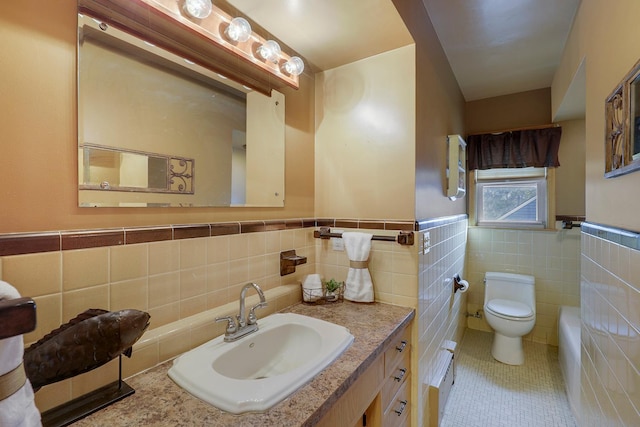 bathroom with tile patterned floors, toilet, tile walls, wainscoting, and vanity