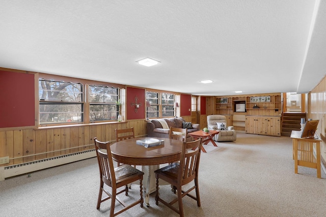 dining space featuring stairway, light colored carpet, a wainscoted wall, and a baseboard radiator