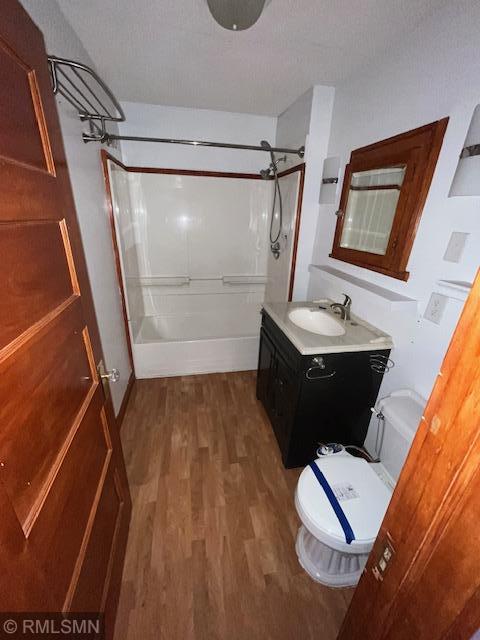 full bathroom featuring  shower combination, vanity, wood-type flooring, a textured ceiling, and toilet