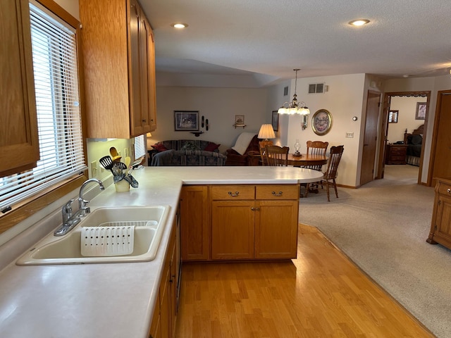 kitchen with sink, an inviting chandelier, decorative light fixtures, light colored carpet, and kitchen peninsula