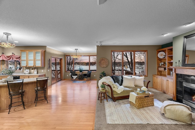 living room with a textured ceiling, a tiled fireplace, baseboards, and light wood-style floors