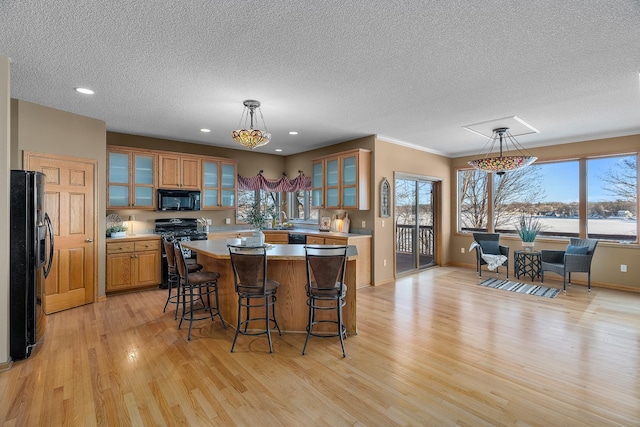 kitchen with a center island, brown cabinets, light countertops, glass insert cabinets, and black appliances