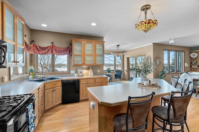 kitchen featuring decorative light fixtures, light countertops, glass insert cabinets, a sink, and black appliances