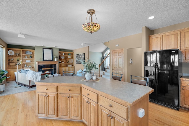 kitchen featuring a tiled fireplace, open floor plan, a center island, hanging light fixtures, and black fridge