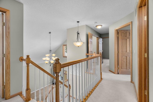 hall with a chandelier, light colored carpet, a textured ceiling, and an upstairs landing