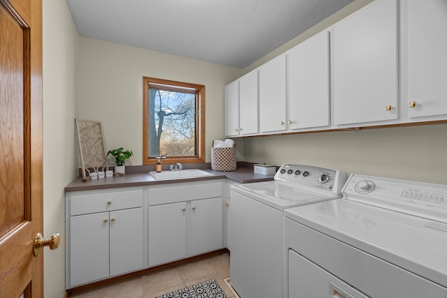 clothes washing area featuring a textured ceiling, light tile patterned flooring, a sink, washer and dryer, and cabinet space