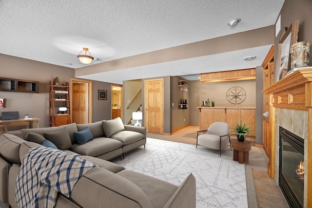 living area with a textured ceiling, baseboards, a tiled fireplace, and light colored carpet