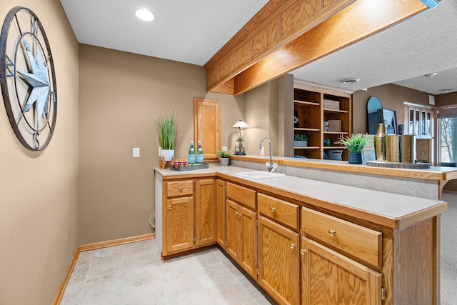 kitchen with a peninsula, a sink, open floor plan, light countertops, and brown cabinetry