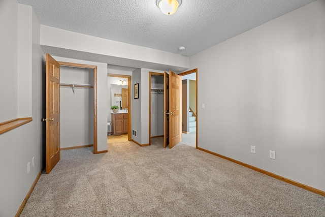 unfurnished bedroom with visible vents, light colored carpet, a textured ceiling, ensuite bath, and baseboards