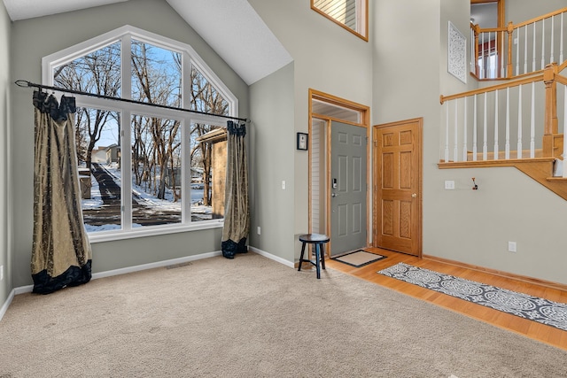 carpeted foyer entrance featuring plenty of natural light, high vaulted ceiling, baseboards, and wood finished floors