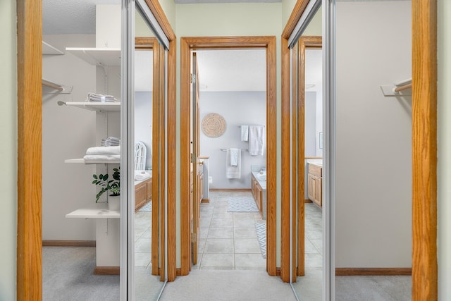corridor with light tile patterned floors, baseboards, and light carpet
