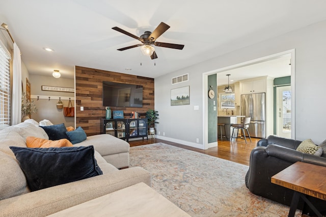 living area with visible vents, an accent wall, wooden walls, wood finished floors, and baseboards