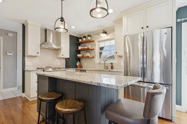 kitchen featuring a kitchen island, hanging light fixtures, wall chimney range hood, freestanding refrigerator, and open shelves