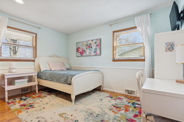 bedroom featuring wood finished floors, visible vents, a textured ceiling, and multiple windows