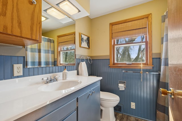 bathroom with a healthy amount of sunlight, a wainscoted wall, toilet, and vanity