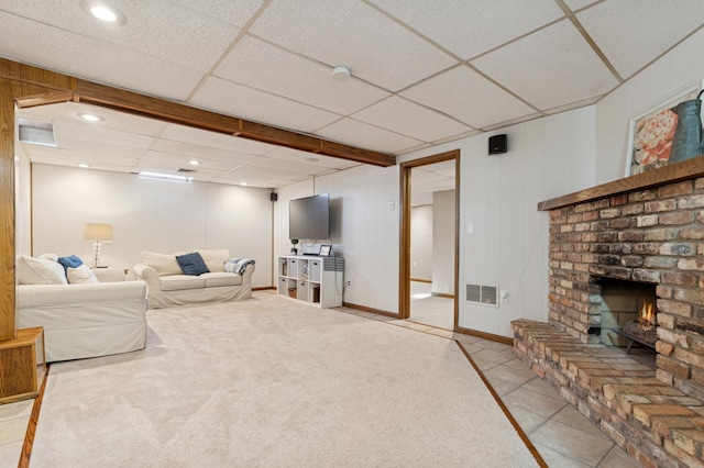 living room featuring light tile patterned floors, baseboards, visible vents, a drop ceiling, and a fireplace