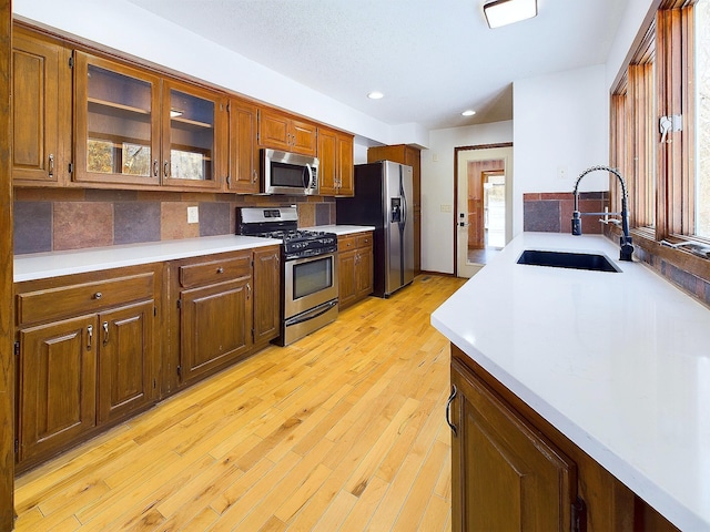 kitchen with sink, a textured ceiling, light wood-type flooring, appliances with stainless steel finishes, and decorative backsplash