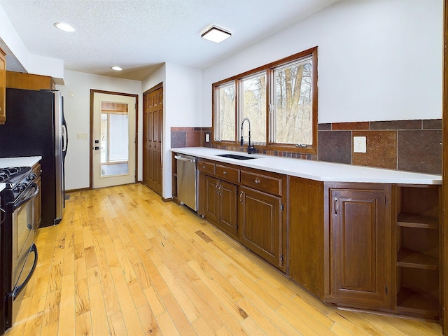 kitchen featuring sink, light wood-type flooring, decorative backsplash, stainless steel appliances, and a textured ceiling