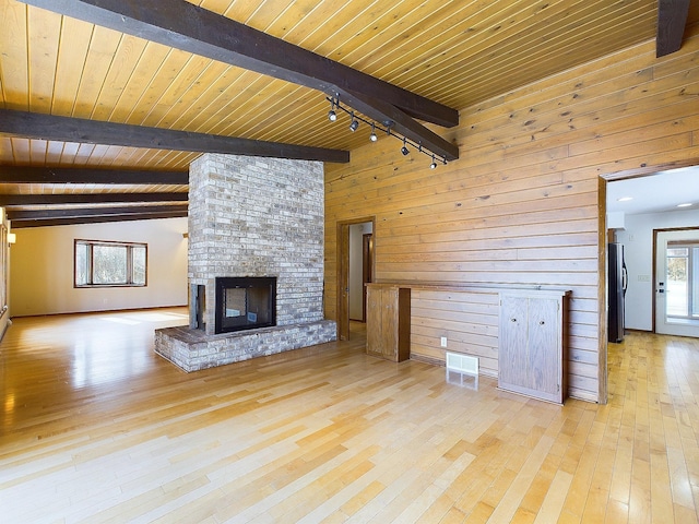 unfurnished living room featuring a brick fireplace, wooden walls, a healthy amount of sunlight, and light wood-type flooring