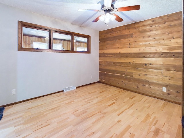 empty room featuring ceiling fan, wood walls, a textured ceiling, and light hardwood / wood-style flooring