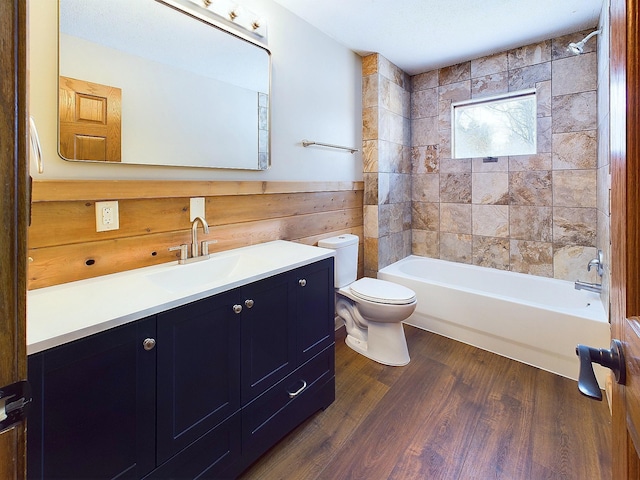 full bathroom with tiled shower / bath combo, wooden walls, vanity, wood-type flooring, and toilet