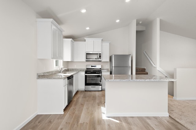 kitchen with light stone counters, stainless steel appliances, a kitchen island, and white cabinets