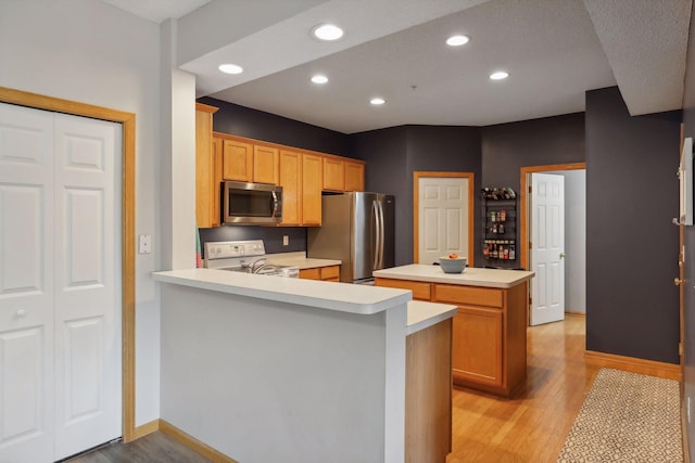 kitchen featuring a center island, light hardwood / wood-style floors, kitchen peninsula, and appliances with stainless steel finishes