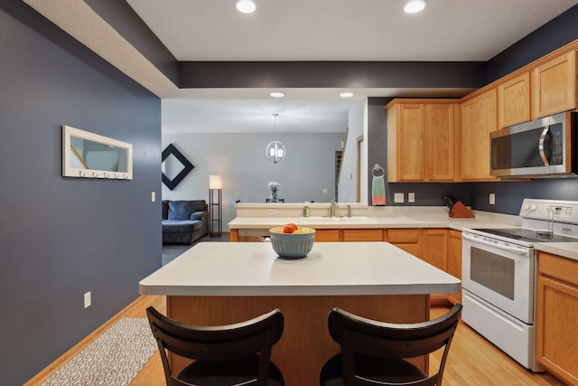 kitchen featuring sink, a breakfast bar, white range with electric stovetop, light hardwood / wood-style floors, and decorative light fixtures