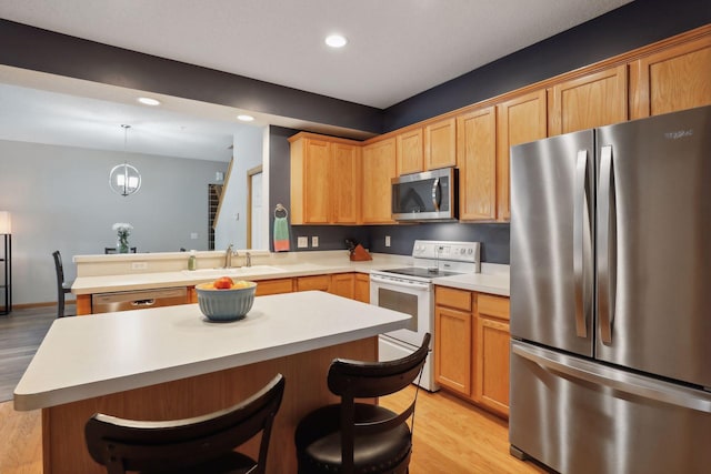 kitchen featuring sink, a breakfast bar area, appliances with stainless steel finishes, light hardwood / wood-style floors, and decorative light fixtures