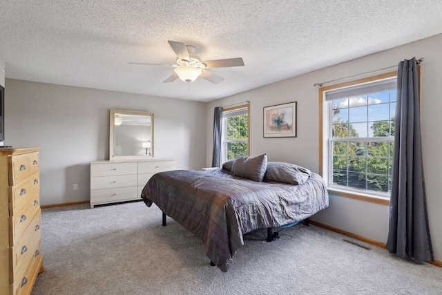 bedroom with ceiling fan, light colored carpet, and a textured ceiling