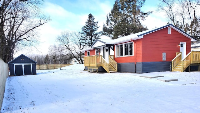 view of snow covered exterior featuring a storage unit, a detached garage, fence, and an outdoor structure