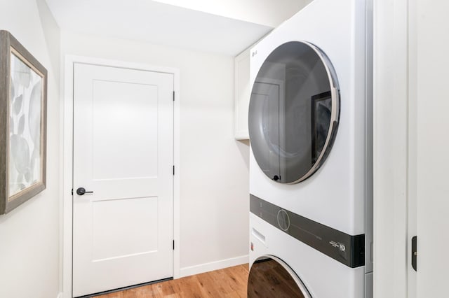 laundry room featuring stacked washing maching and dryer and light hardwood / wood-style floors