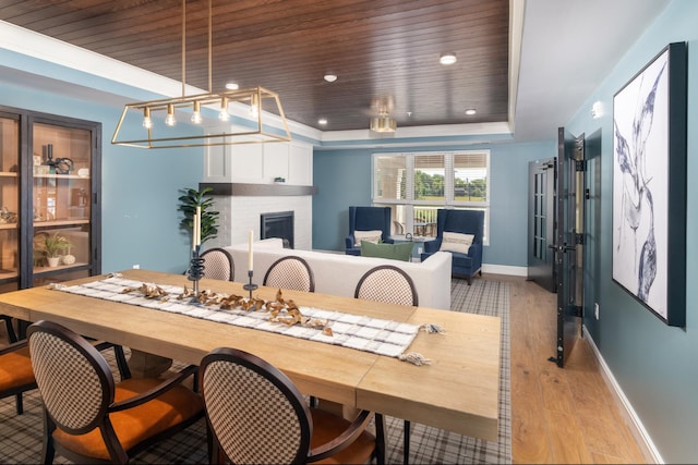 dining area with wood ceiling, a raised ceiling, a brick fireplace, and light wood-type flooring