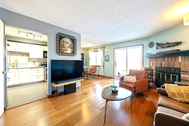 living area featuring light wood-style floors, a brick fireplace, and a textured ceiling